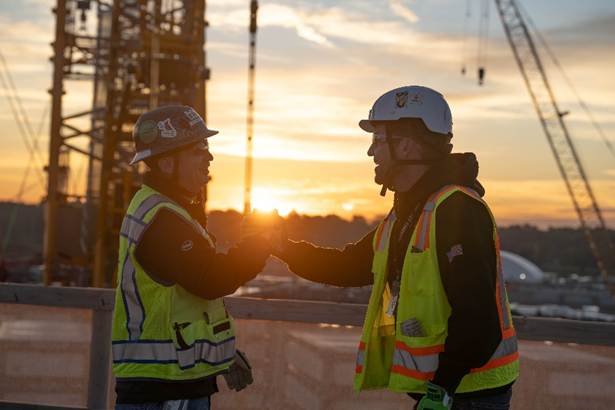 An Intel Foundry employee and a Bechtel construction worker stand together at sunset on a construction site.